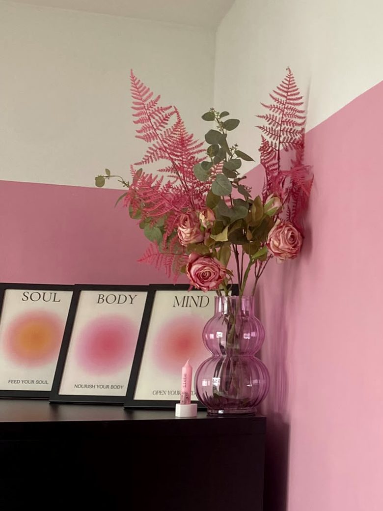 Ecke mit rosa Wand, Vase mit Farn und Rosen und drei Bildern mit den Worten Soul, Body, Mind